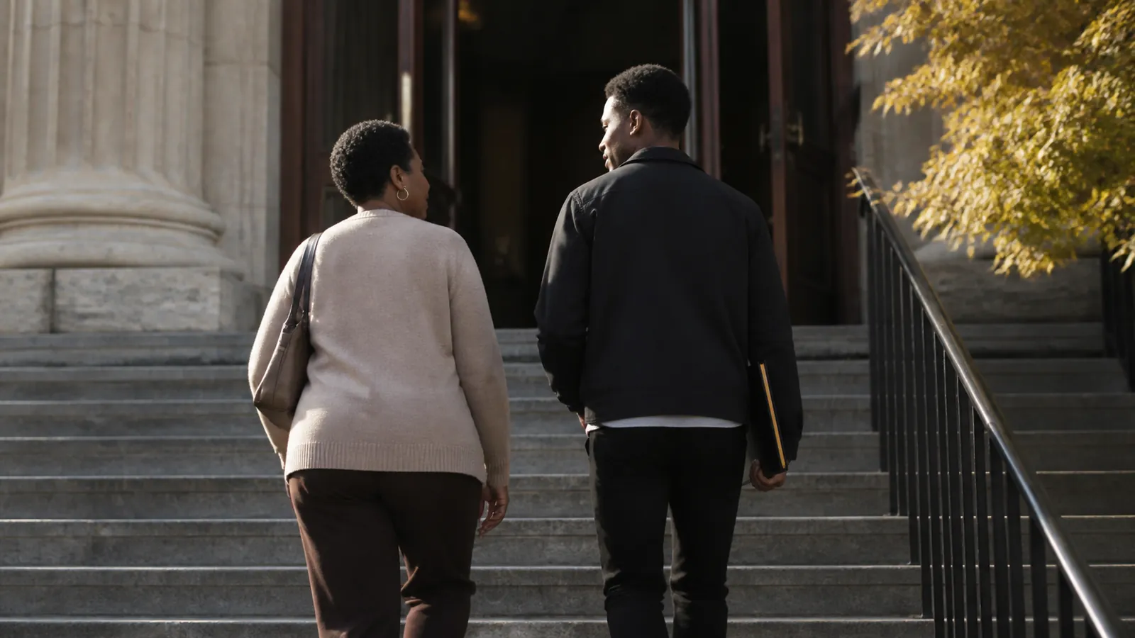 Mother and adult son walking up courthouse steps together carrying one slim gold-tabbed folder